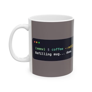 May include: A white ceramic mug featuring a dark grey rectangular graphic that mimics a computer terminal window. The graphic displays the text (venv) $ coffee --refill followed by the text Refilling mug... done. in white, green, and yellow.