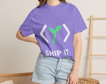 Może przedstawiać: Jasnofioletowy t-shirt z krótkim rękawem z białą grafiką przedstawiającą nawiasy kątowe otaczające ikonę zielonego kiełka. Pod grafiką znajduje się napis SHIP IT. białymi wielkimi literami z małą zieloną kropką na końcu.