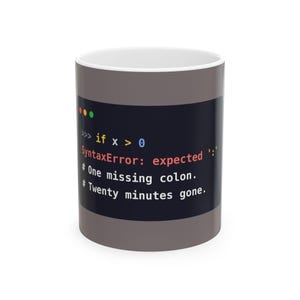 May include: A grey ceramic mug featuring a dark rectangular graphic with code text that reads: if x > 0, SyntaxError: expected ':', # One missing colon., # Twenty minutes gone. The mug has a white interior and a cylindrical shape with a smooth finish.