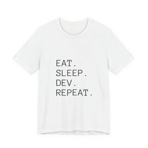 May include: White t-shirt featuring the text "EAT. SLEEP. DEV. REPEAT." in black, centrally placed. The shirt has a round neck and short sleeves. A casual, everyday wear tee.