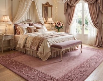 May include: A rectangular area rug in a dusty rose color featuring a decorative border with an embossed floral scroll pattern. The rug is placed in a bedroom setting with a bed, a canopy, a velvet bench, and curtains in coordinating shades.
