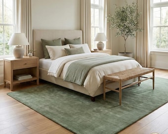 Puede incluir: Una habitación con una cama con ropa de cama color crema y detalles en verde salvia. Un banco tejido se encuentra al pie de la cama, y una alfombra verde salvia cubre el suelo. Mesitas de noche de madera con lámparas a ambos lados de la cama.