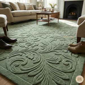 May include: A sage green area rug with a raised floral pattern. The rug is in a living room setting, with a sofa, chairs, and a fireplace visible in the background. The rug's design features swirling leaves and vines.