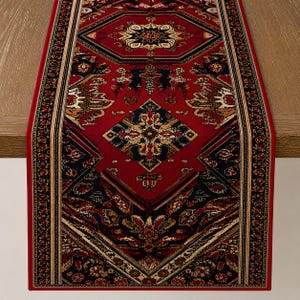May include: A rectangular table runner featuring a deep red background with intricate black, cream, and gold geometric and floral patterns. The design includes a central diamond motif and a symmetrical border, creating a detailed textile piece.