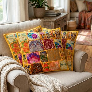 May include: Three patchwork throw cushions in a variety of colours, including red, yellow, blue, and purple. The cushions have a yellow border and are arranged on a beige armchair, creating a cosy and colourful home decor scene.