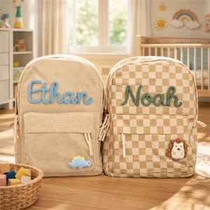 May include: Two beige backpacks, one corduroy and one checkered, are displayed. The corduroy backpack has the name "Ethan" in blue script, a small blue dinosaur, and a front pocket. The checkered backpack has the name "Noah" in green script and a hedgehog patch.