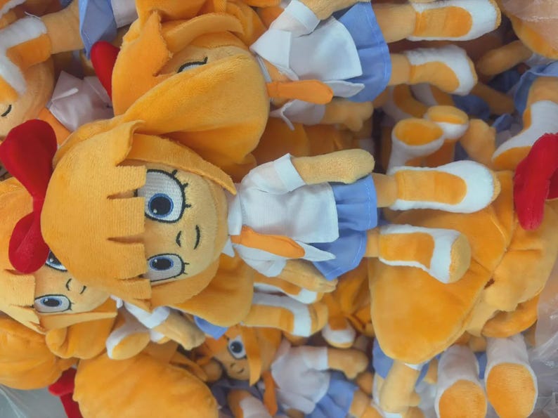 May include: A pile of plush dolls with yellow hair, blue eyes, and orange beaks. The dolls wear white shirts and blue skirts. Some dolls have red bows. The dolls are made of soft, plush material.