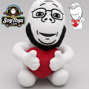 May include: A soft toy depicting a meme character with a white head, black beard, and spectacles. The toy is holding a red heart. The SoyToys.com logo is visible in the upper left corner.