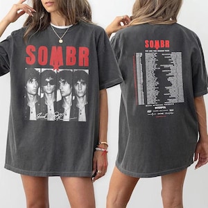 May include: Dark gray t-shirt featuring the band name "SOMBR" in red block letters above a black and white image of four band members. The shirt also has the band's signature and tour dates printed on the back.