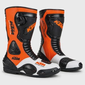 Könnte beinhalten: Paar orangefarbene, schwarze und weiße Motorrad-Rennstiefel. Die Stiefel tragen das KTM Racing Team-Logo und bestehen aus Leder und synthetischen Materialien. Die Stiefel haben verstärkte Bereiche zum Schutz und ein schlankes Design.