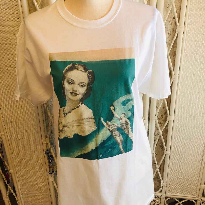 May include: White t-shirt featuring a vintage-style graphic. The graphic includes a portrait of a woman in a dress and a scene of two people in swimwear. The background is teal and beige.