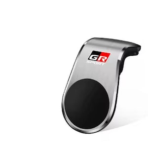 Puede incluir: Accesorio para coche plateado y negro con el texto "GR SPORT" en rojo y negro. El accesorio tiene un diseño curvo con un área negra circular en la parte inferior.