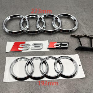 May include: Chrome Audi emblems and S3 badges. The larger emblem measures 273mm, and the smaller one is 192mm. The S3 badges have a red background with silver lettering. The Audi emblems feature the iconic four interlocking rings.