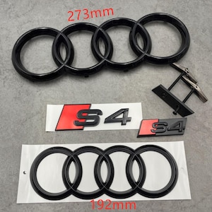 May include: Black car emblem set featuring the Audi rings logo, measuring 273mm and 192mm, along with S4 badges with red accents. Includes a pair of black cufflinks.