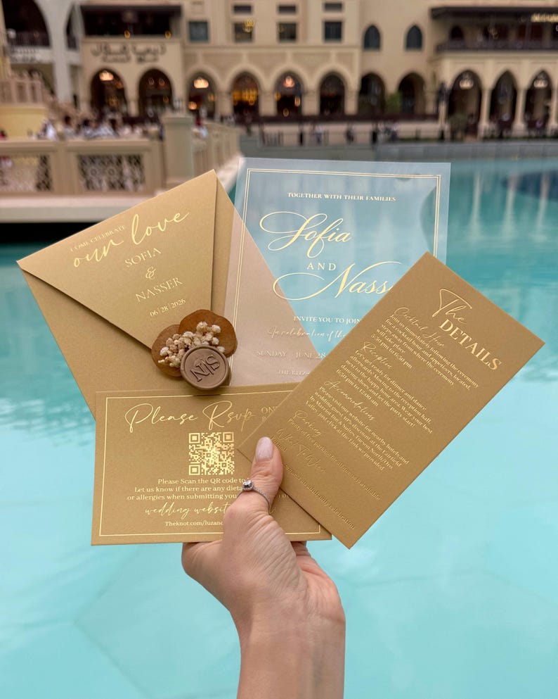 May include: Gold wedding invitation suite with calligraphy text. The suite includes an envelope, invitation, RSVP card, and details card. The envelope is sealed with a wax stamp. The invitation text includes the names Sofia and Nasser.