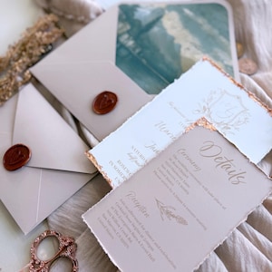 May include: Wedding invitation suite featuring a light beige color scheme with gold accents. Includes invitation cards with torn edges, envelopes sealed with wax stamps, and decorative scissors. The invitation details are printed in a delicate font.