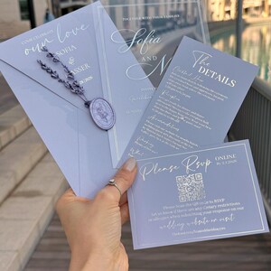 May include: A collection of elegant wedding invitations in shades of lavender and silver. The invitations include details such as the names "Sofia and N", RSVP information, and the wedding date. The design features a wax seal and decorative script.