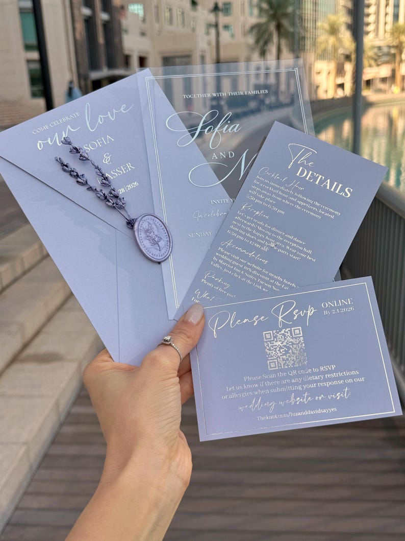 May include: A collection of elegant wedding invitations in shades of lavender and silver. The invitations include details such as the names "Sofia and N", RSVP information, and the wedding date. The design features a wax seal and decorative script.