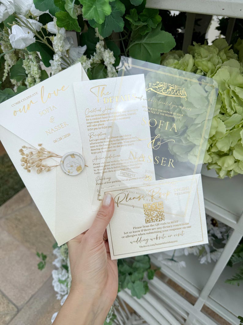 May include: Wedding invitation suite featuring a cream-colored envelope with gold foil text and a wax seal. Includes transparent cards with gold text detailing event information and a QR code for RSVP. The suite is for Sofia & Nasser.