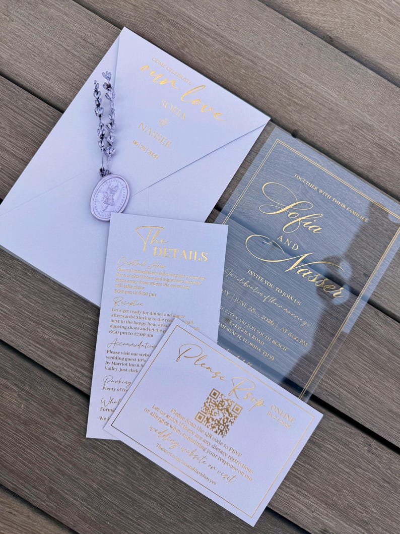 May include: A collection of wedding stationery, including an invitation, RSVP card, and details card. The invitation features gold foil lettering on a clear acrylic background. The stationery is light blue and white, with gold accents and a lavender embellishment.