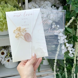 May include: Wedding invitation featuring the names Sofia & Nasser. The invitation is on a cream-colored envelope with a wax seal and dried flowers. A clear overlay displays the names and event details.