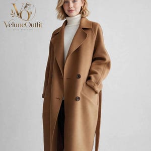 May include: A camel-colored double-breasted wool coat featuring wide lapels, long sleeves, and two dark buttons on the front. The coat is worn over a white ribbed turtleneck sweater. The logo VeluneOutfit is visible in the top left corner.