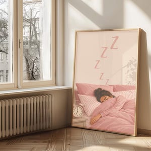 May include: A framed art print shows a person asleep in a pink bed, with the letter "Z" repeated above. A small alarm clock is on the bedside table. The artwork is in a room with a window and a radiator.