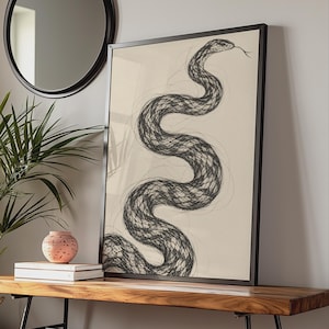 May include: A framed wall art print featuring a black ink sketch of a winding snake on a light beige background. The snake is depicted with a detailed, cross-hatched texture and a visible tongue, enclosed within a thin black rectangular frame.