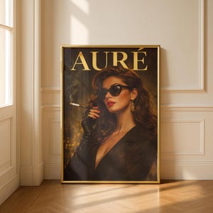 May include: A framed art print with the word "AURÉ" in gold. The image shows a woman in sunglasses, wearing a black jacket and gloves, holding a cigarette. She has red lipstick and gold earrings. The print is in a gold frame.
