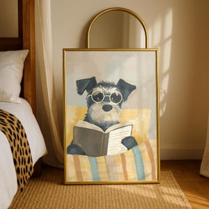 Könnte beinhalten: Ein gerahmter Kunstdruck mit einem Schnauzer-Hund, der eine Brille trägt und ein Buch liest. Der Hund liegt auf einem gelben Kissen und ist mit einer gestreiften Decke bedeckt. Der goldene Rahmen und das Kunstwerk werden in einem Schlafzimmer gezeigt.