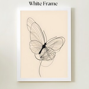 May include: A framed wall art piece featuring a black line drawing of a butterfly on a light beige background. The artwork is enclosed in a simple white frame. The butterfly design consists of thin, overlapping lines forming the wings.