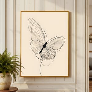 May include: A rectangular wall art print featuring a black line drawing of a butterfly with delicate, overlapping wing patterns on a solid cream-colored background, encased in a thin, metallic gold frame that highlights the artwork's clean lines.