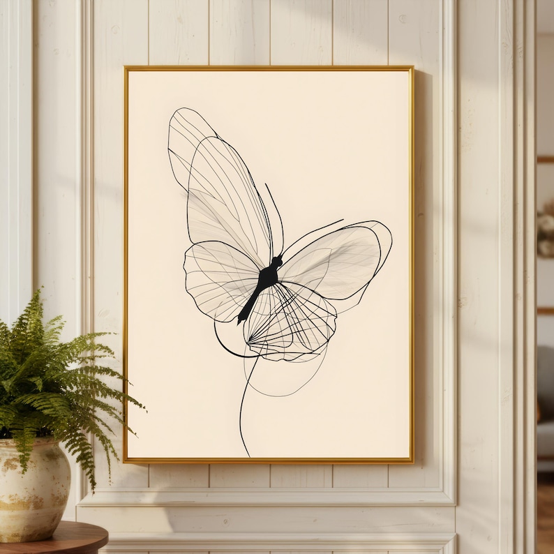 May include: A rectangular wall art print featuring a black line drawing of a butterfly with delicate, overlapping wing patterns on a solid cream-colored background, encased in a thin, metallic gold frame that highlights the artwork's clean lines.