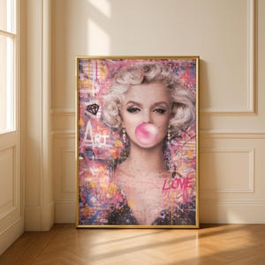 May include: A framed art print featuring a portrait of Marilyn Monroe blowing a bubblegum bubble. The artwork has a colorful, graffiti-style background with the words "ART" and "LOVE" visible. The frame is gold.
