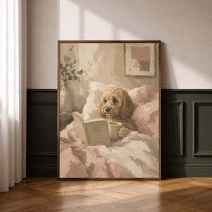 May include: A framed print showing a dog in bed, reading a book and holding a mug. The artwork uses soft, muted tones of pink, beige, and white, creating a cosy and inviting atmosphere. The dog is a light brown colour.