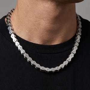 Peut inclure: Un collier argenté en forme de chaîne de vélo. Le collier est composé de maillons métalliques entrelacés. Le design de la chaîne est distinctif. Un accessoire unique.