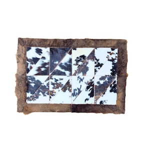 May include: A rectangular rug constructed from triangular patches of cowhide featuring a mix of white, black, and brown spotted patterns. The central geometric design is framed by a solid, textured brown fur border along all four edges.