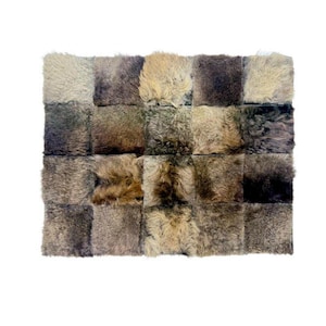 May include: A rectangular rug composed of multiple square patches of varying shades of brown and tan fur. The patches are arranged in a grid pattern, creating a textured surface. The rug appears to be made of natural materials.