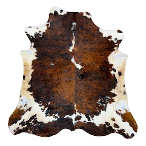 May include: A cowhide rug with a natural pattern of brown, white, and black spots. The rug has an irregular shape and a soft, textured appearance. The hide is likely from a cow and is suitable for use as a floor covering or decorative item.