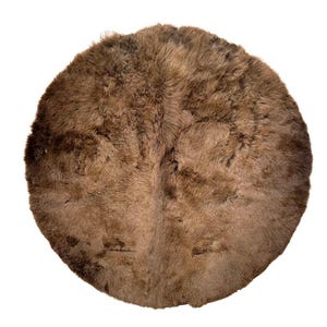 May include: A round, brown rug with a shaggy texture. The rug is made of a soft, fur-like material and has a natural, earthy appearance. The rug is circular in shape and would be suitable for a living room or bedroom.