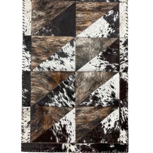 May include: A rectangular cowhide rug with a patchwork design. The rug features geometric shapes in shades of brown, black, and white. The edges are stitched with a contrasting thread. The rug is designed for home decor.