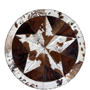 May include: Round cowhide rug featuring a large star design. The rug is made of brown, white, and tan cowhide patches stitched together. The star is the focal point, with a dark brown center and lighter brown and white sections.