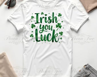 Può includere: T-shirt bianca con la scritta "Irish you Luck" in verde, circondata da trifogli verdi. La maglietta è presentata su una superficie bianca, con occhiali da sole e capi di abbigliamento sullo sfondo.
