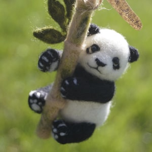 May include: A handmade panda bear figurine, crafted from white and black felt, clinging to a bamboo stalk with green leaves. The panda has a smiling face and is suspended by a string. A small tag is attached.