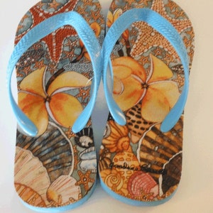 May include: A pair of blue flip-flops with a colorful tropical print featuring seashells, starfish, and flowers. The flip-flops have a blue strap and a brown sole.