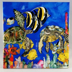 May include: A colorful tile featuring a vibrant underwater scene with multiple sea turtles, angelfish, and coral. The tile has a blue background with a variety of colors in the coral and fish.