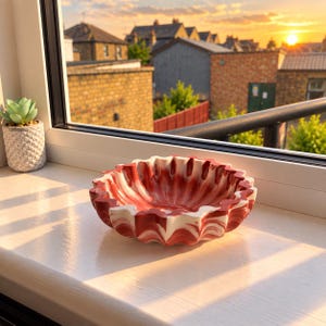 May include: A round, scalloped-edge bowl featuring a marbled pattern of deep red and white swirls. Beside it sits a small, light green succulent plant housed in a textured, light grey pot with a repeating diamond pattern on its exterior surface.