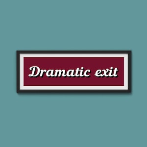 May include: A framed sign with the words "Dramatic exit" in a white, cursive font with a black shadow. The sign has a burgundy background and a black frame, set against a teal wall.