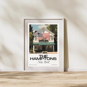 May include: A framed print featuring a white building with an American flag and a green awning. The text "THE HAMPTONS New York" is displayed below the image, with "Ralph Lauren Store" and "Southampton" below.