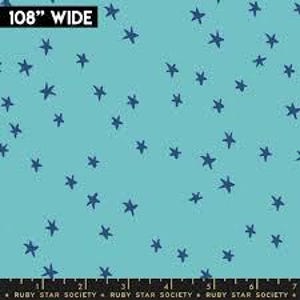 May include: A light blue fabric featuring a scattered pattern of dark blue stars. The top left corner displays the text 108" WIDE, and the bottom edge features a black border with the repeating text RUBY STAR SOCIETY.